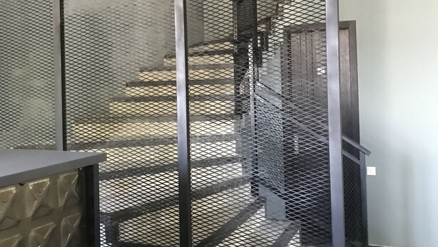 A staircase with a metal mesh railing and a textured wall. - Hotel Aguna (Kutaisi)