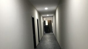A narrow, dimly lit hallway with dark wooden flooring and white walls. - Hotel Aguna (Kutaisi)