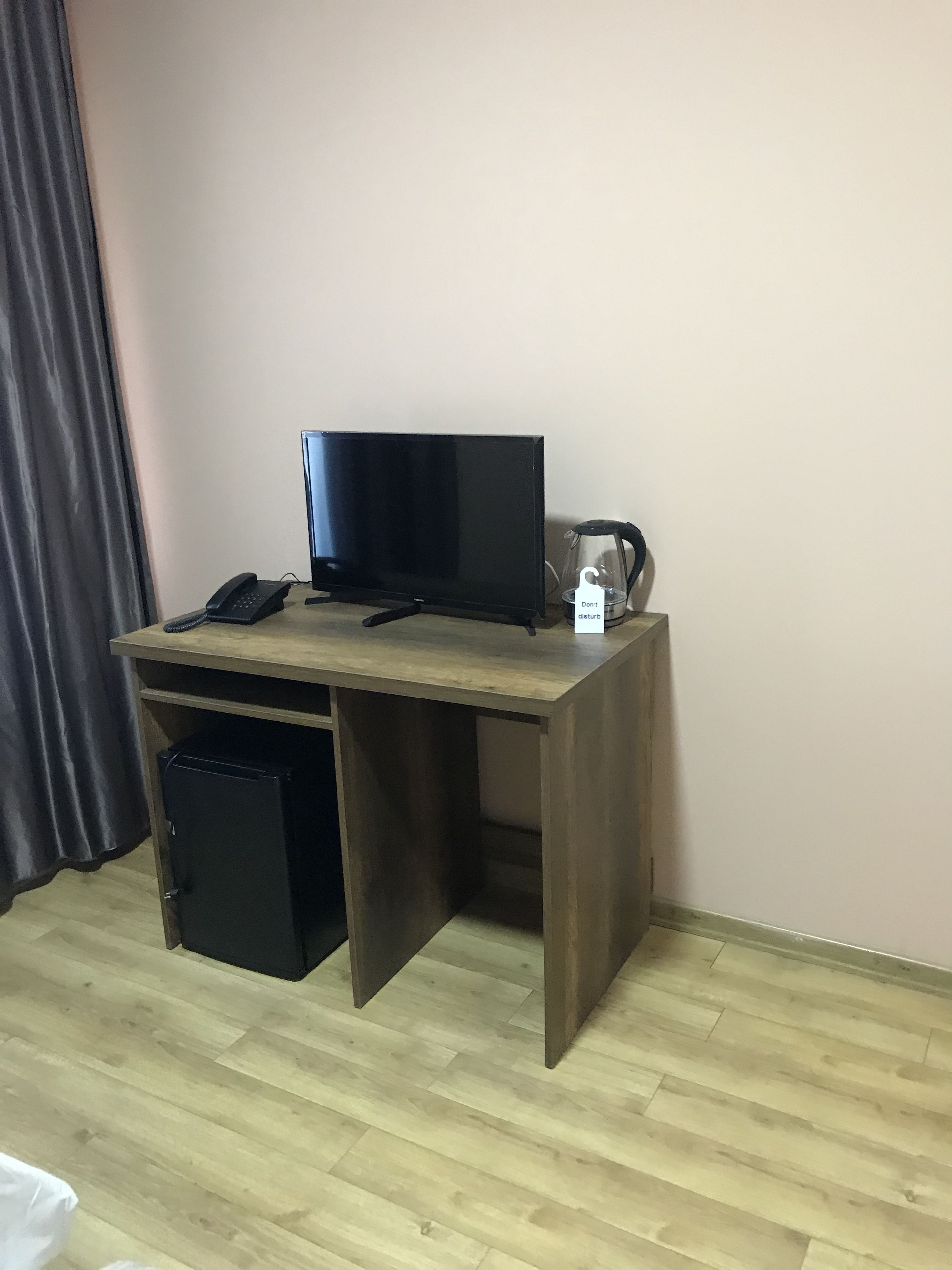 A small, dark wooden desk with a flat-screen TV, a telephone, and a coffee maker.