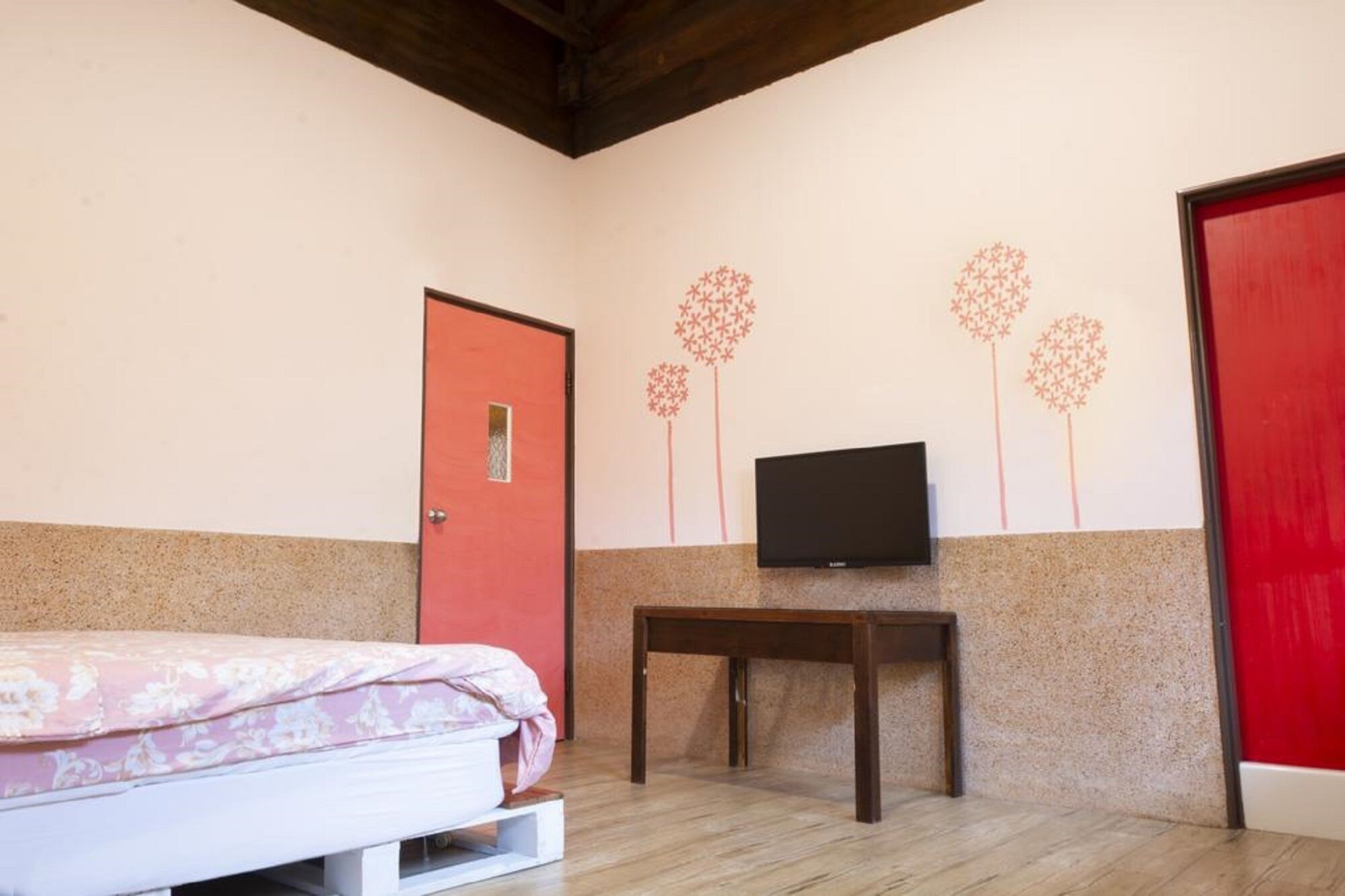 Een slaapkamer met een bed, een televisie op een standaard en een rode deur.
