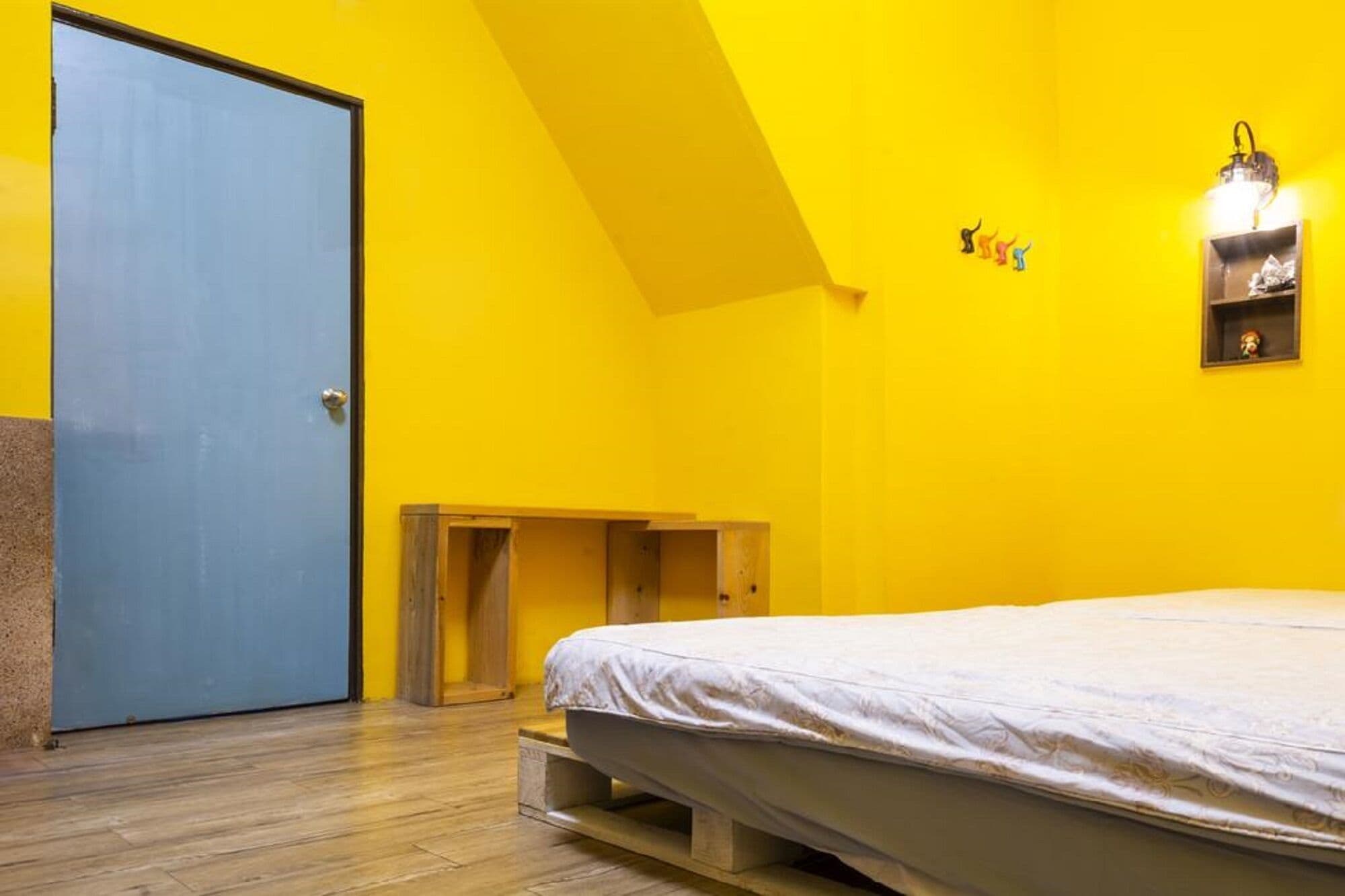 A room with a bed, a blue door, and a yellow wall.