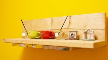 Een plank met drie mokken en twee kleine decoratieve objecten voor een gele achtergrond.