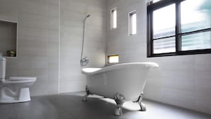 A modern bathroom with a freestanding bathtub, a toilet, and a shower. There are three small windows providing natural light. - OAOA Anping House (Tainan)