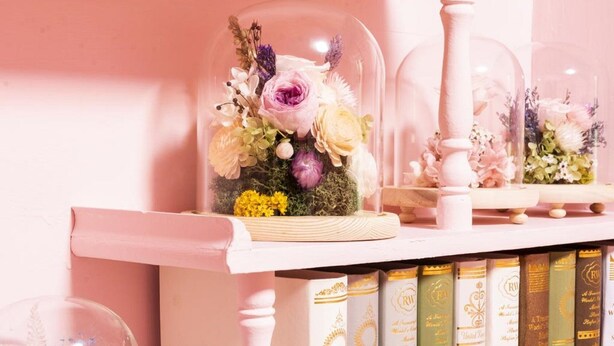 A shelf with a glass dome containing a floral arrangement, surrounded by books. - OAOA Anping House (Tainan)