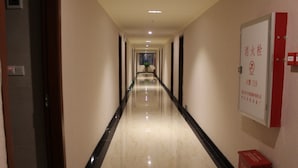 Un pasillo de hotel con piso de mármol pulido, puertas a ambos lados y un letrero de seguridad contra incendios en la pared derecha.