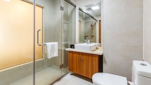 Un baño moderno con ducha de vidrio, tocador de madera y váter blanco.