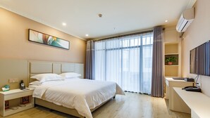 Una habitación de hotel moderna con una cama grande, mesitas de noche, un escritorio y un amplio ventanal con cortinas.