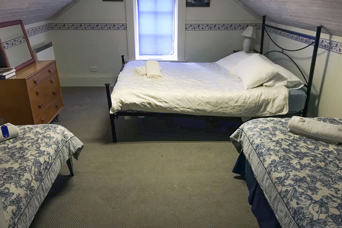 Ett sovrum med en enkelsäng, två sängbord, en byrå och ett fönster med utsikt över en byggnad.