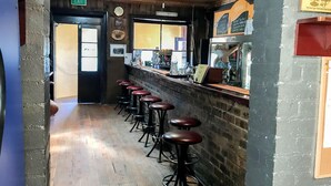 A bar area with wooden flooring, a brick wall, and a counter with stools. - Bushranger Hotel (Collector)