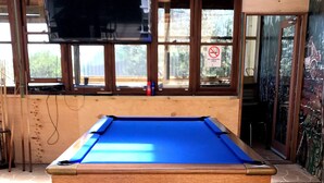 A pool table with a blue felt surface, wooden legs, and a pocket at the bottom. - Bushranger Hotel (Collector)