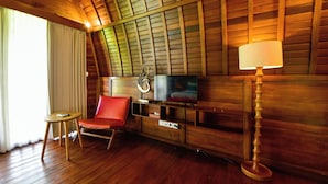 A cozy room with wooden walls, a television, a red chair, a small table, and a lamp. - The Lumbung Wood Villa (Seminyak)