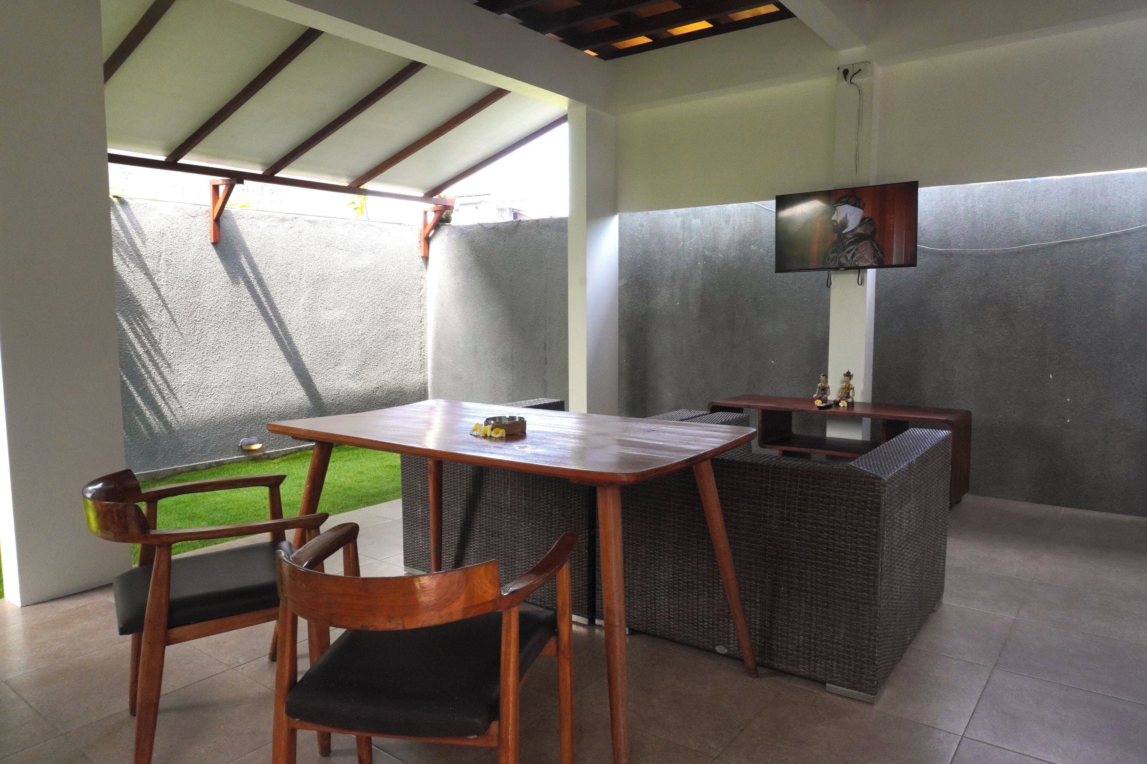 A dining area with a table, chairs, a television, and a small garden view.