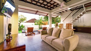 A spacious living area with a sofa, chairs, and a wooden table. There is a ceiling fan, a staircase, and a view of the outdoors. - The Lumbung Wood Villa (Seminyak)