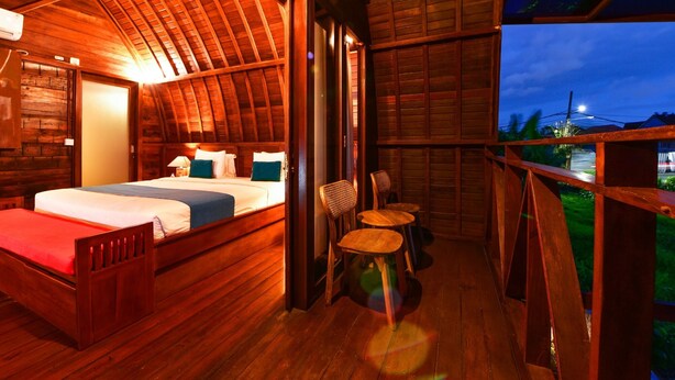A wooden cabin with a bed, two chairs, and a balcony with a view. - The Lumbung Wood Villa (Seminyak)
