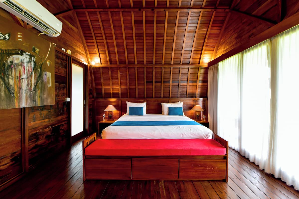 Um quarto com painéis de madeira, uma cama grande, um quadro na parede e uma janela com cortinas.