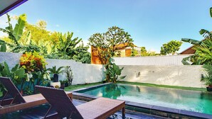 A pool area with lounge chairs, a wooden deck, and lush greenery. - The Lumbung Wood Villa (Seminyak)