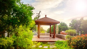 A gazebo with a wooden roof and bench, surrounded by lush greenery and a stone pathway. - Hundred Hotel (Qingdao)