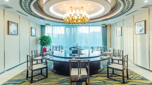 A modern conference room with a round table, chairs, a chandelier, and framed pictures on the walls. - Hundred Hotel (Qingdao)