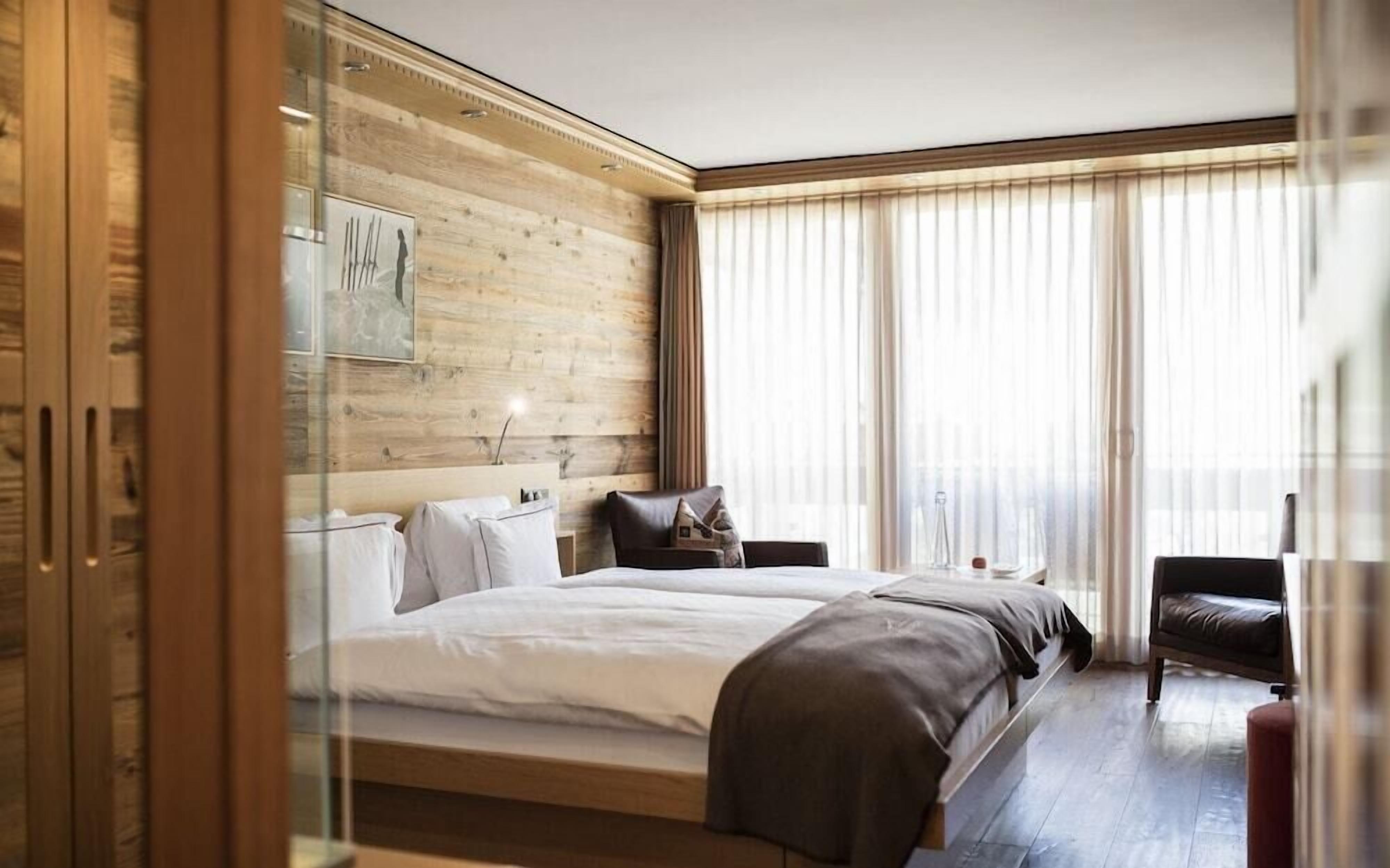 A modern hotel room with a wooden accent wall, a large bed, a bedside table, and a chair.