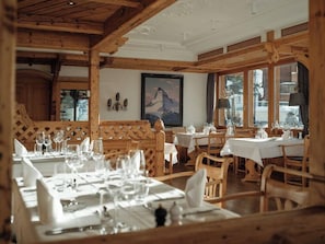A restaurant with wooden beams, tables set for dining, and a mountain painting on the wall.