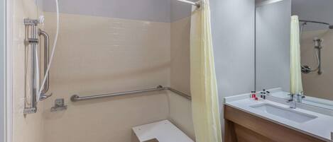 A bathroom with a shower, grab bars, a white sink, and a mirror.