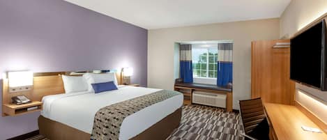 A hotel room with a large bed, a desk with a chair, a television, and a window with curtains.