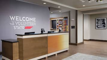 A reception desk with a 'Welcome to Volunteer State' sign, a self-service kiosk, and a 'Suite Shop' sign.