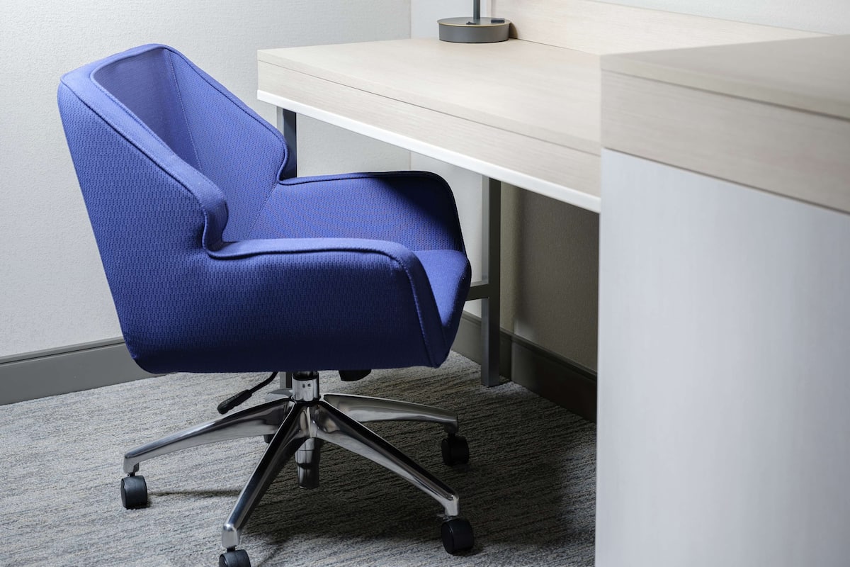 A blue office chair with a five-star base, positioned in front of a desk with a light-colored surface and a black lamp.