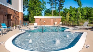 A swimming pool with a brick building in the background, surrounded by trees.