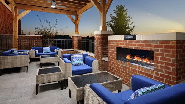 An outdoor patio area with wicker furniture, a brick fireplace, and a ceiling fan.