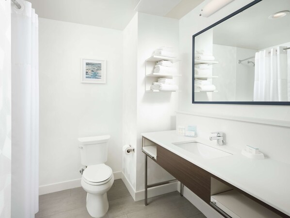 A modern bathroom with a white toilet, a sink with a mirror, and shelves with folded towels.