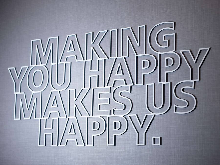 Pared metálica com texto em relevo que diz 'MAKING YOU HAPPY MAKES US HAPPY'.