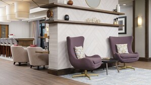 A modern lobby with two purple armchairs, a wooden reception desk, and a wall-mounted mirror.