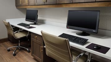 A modern office space with two desks, each equipped with a computer monitor, keyboard, and mouse. The room features wooden flooring, a white desk, and brown leather chairs.
