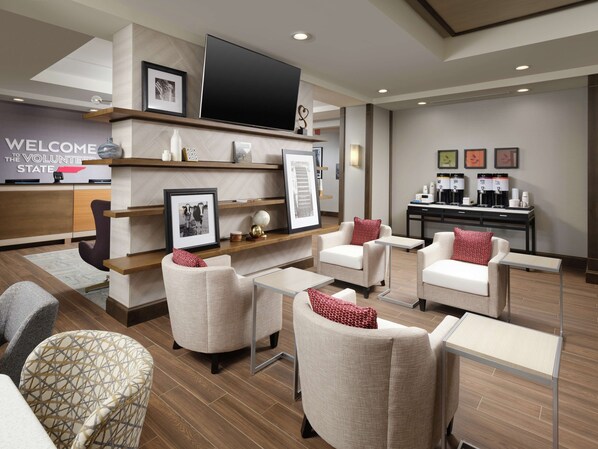 A modern lobby with seating areas, a reception desk, and a coffee station.