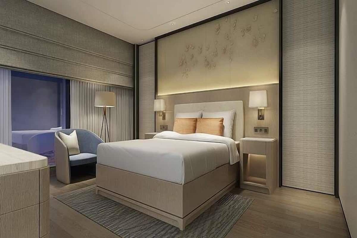 A modern hotel room with a large bed, bedside tables, a chair, and a large window.