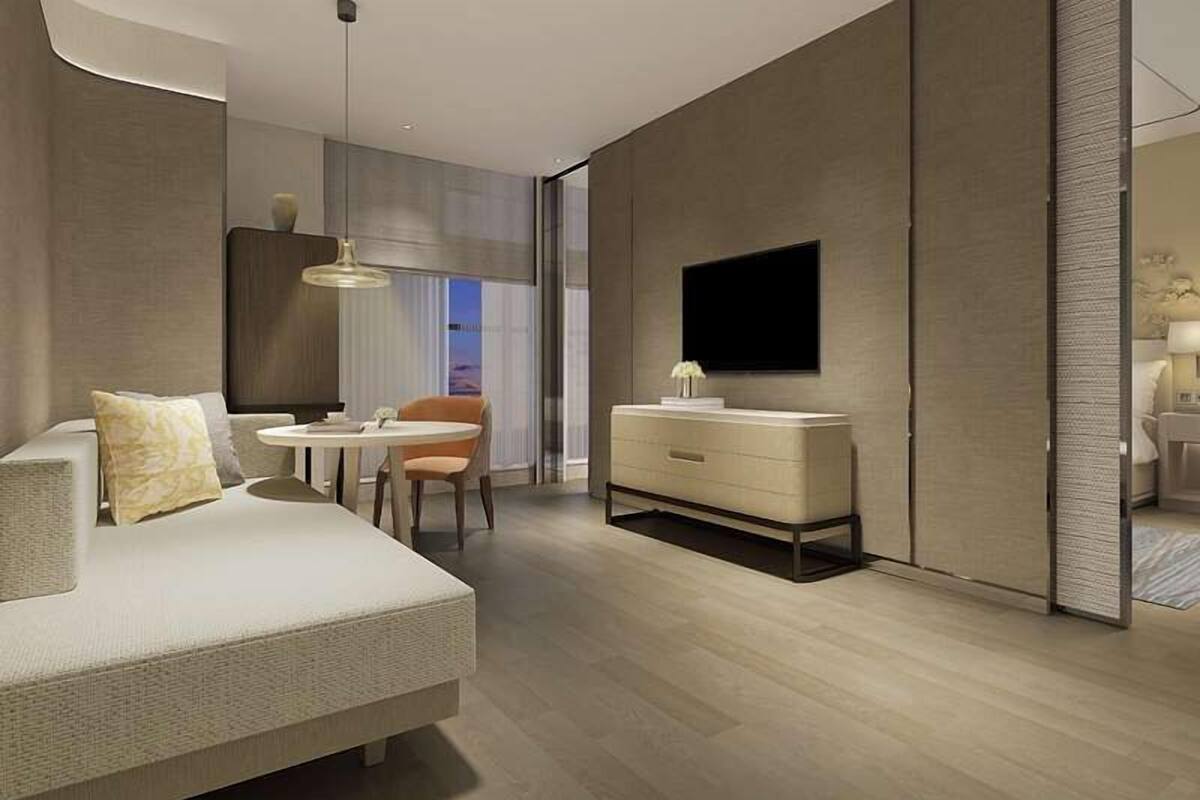 A modern hotel room with a sofa, a small round table, a chair, a bedside table, a TV, and a wardrobe.