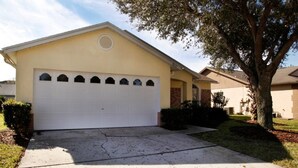 A single-story house with a white garage door, a brick section on the right, and a tree in front. - Ly53763 - Indian Ridge - 4 Bed 2 Baths Villa (Kissimmee)