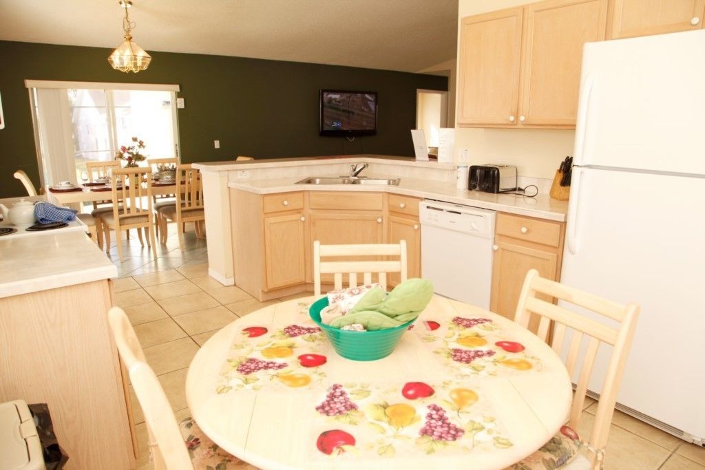 A compact kitchen with a dining area, wooden cabinets, a dishwasher, and a television mounted above the sink.