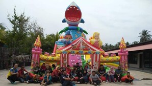 Un grupo de personas reunidas alrededor de una estructura inflable colorida con temática de tiburón y circo.