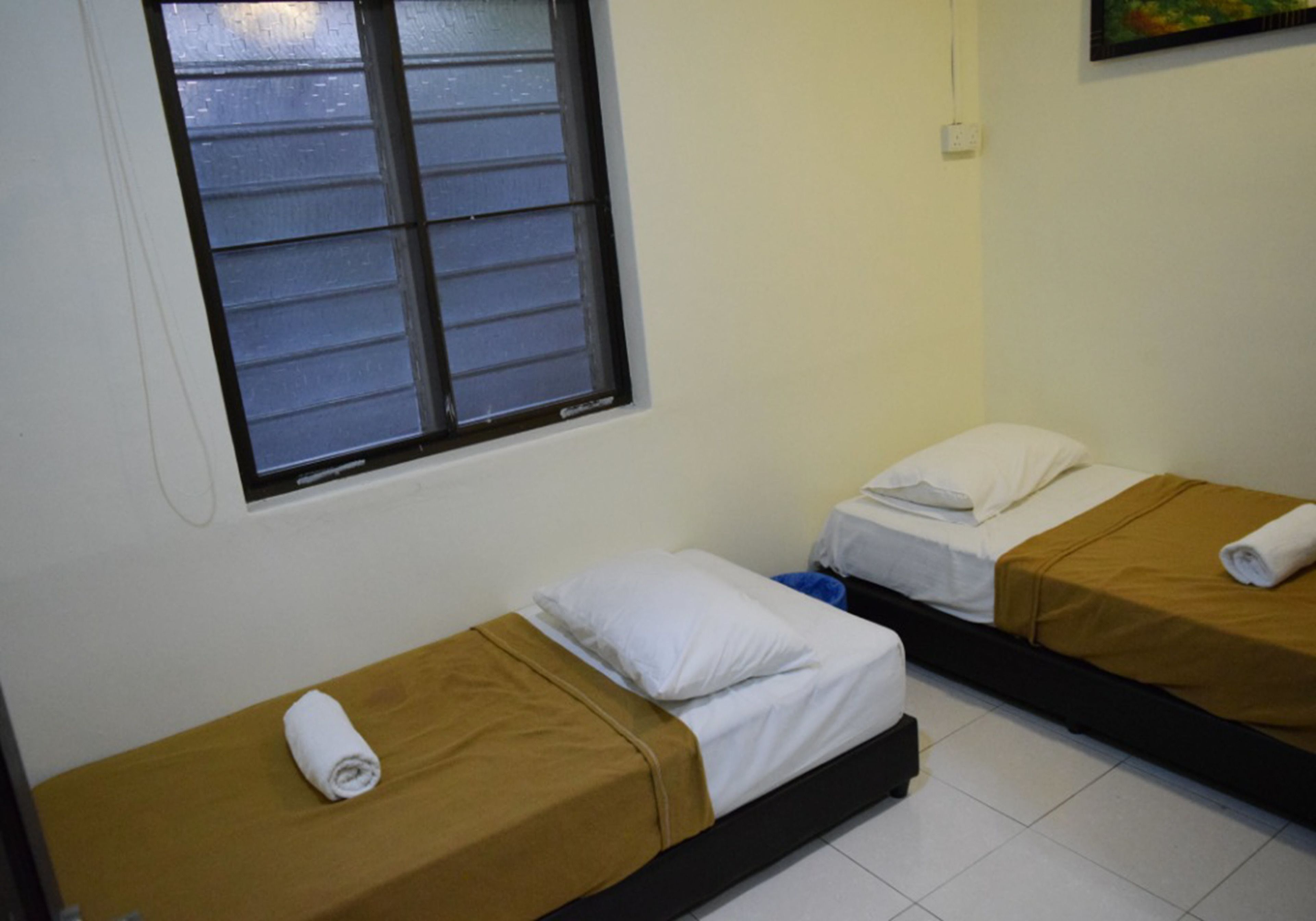 Two single beds with brown bedding, a window with closed blinds, and a white wall.