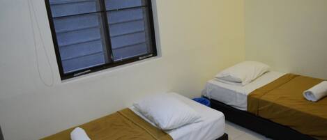 Two single beds with brown bedding, a window with closed blinds, and a white wall.