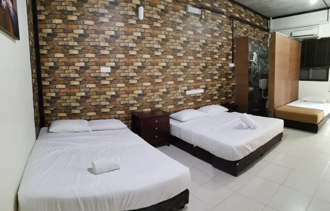 A hotel room with two beds, a brick-patterned wall, a small wooden cabinet, and a window with blinds.