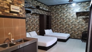 Una habitación de hotel compacta con dos camas individuales, un kitchenette y una pared con diseño de ladrillo.