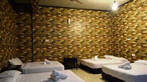 Una habitación con cuatro camas dispuestas en forma de U, cada una con ropa de cama y toallas blancas. Las paredes están cubiertas de un papel tapiz con diseño de ladrillo.