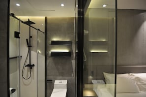 Ein modernes Badezimmer mit einer Duschkabine, einer Toilette und einem Bett mit weißer Bettwäsche.
