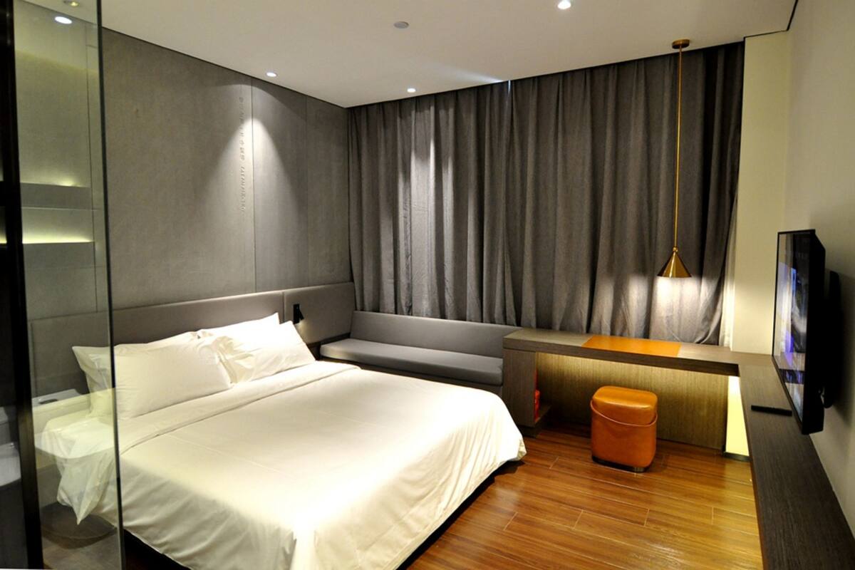 Ein modernes Hotelzimmer mit einem großen Bett, einer Sitzecke, einem kleinen Tisch, einem Fernseher und einem Spiegel.