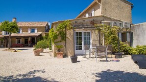 A building with a patio area, outdoor seating, and potted plants. - Mas Julien (Orange)