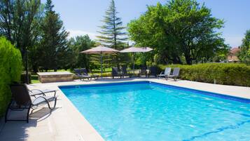 A swimming pool with lounge chairs and umbrellas, surrounded by trees and greenery.