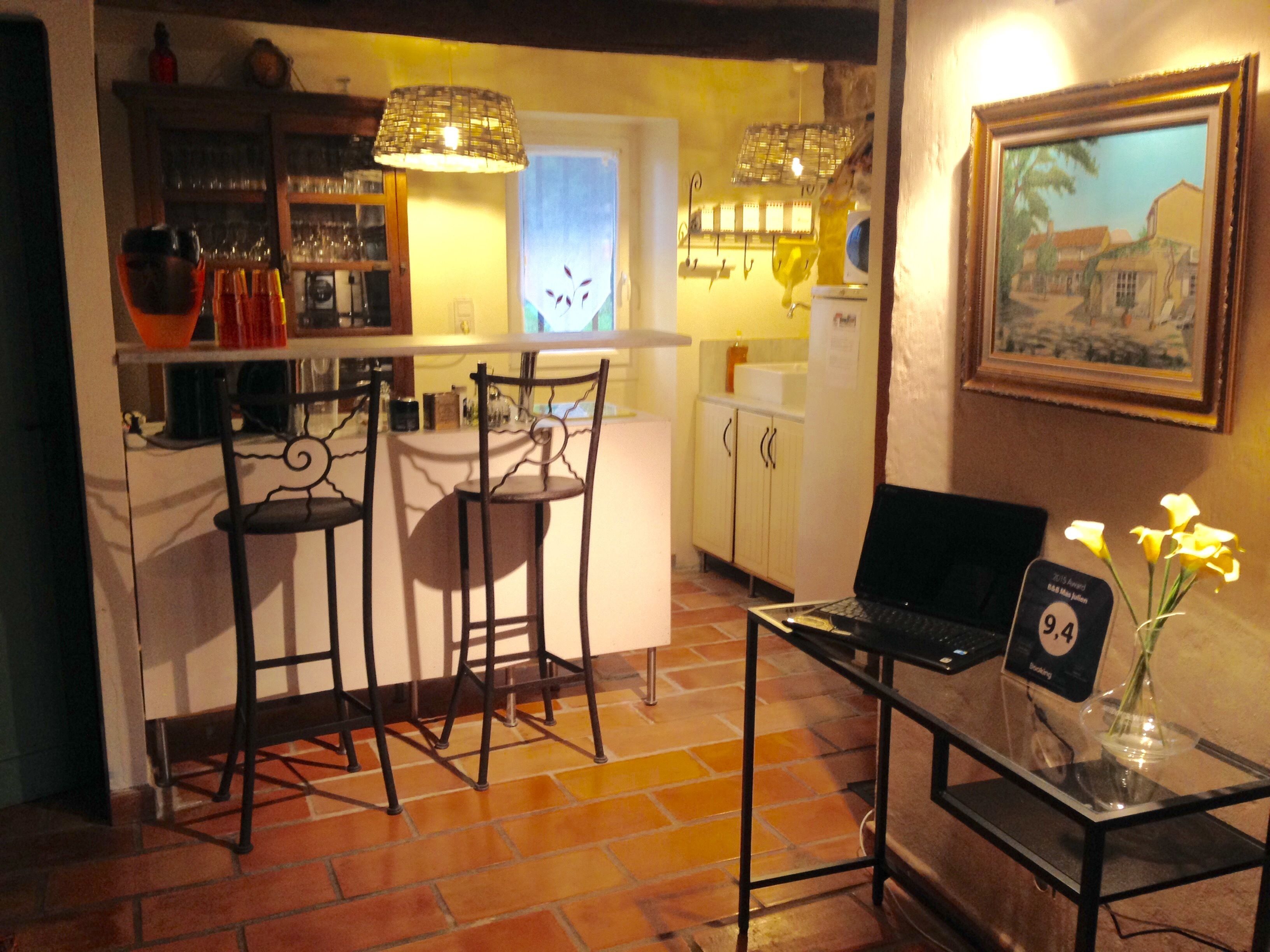Une cuisine chaleureuse avec un coin bar, deux tabourets de bar, une table à plateau en verre ornée d’un vase de fleurs et un tableau encadré accroché au mur.